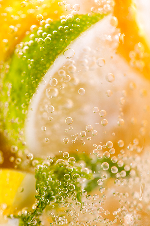 Macro photo of freshly made lemonade with pieces of lime, lemon and bubbles in a glass. Summer refreshing drink