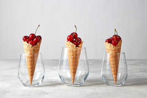 Red ripe juicy cherries at the wafer cones in a three glasses stand on a gray table with copy space. The concept of homemade ice cream.