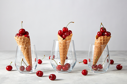The glass cups with crispy waffle cones and ripe red cherries on a gray srone table, background , copy space. Summer concept of homemade cake.