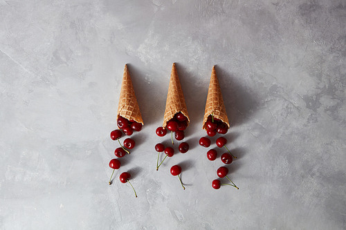 Fresh red cherry in waffle cups for homemade gelato on a gray stone background with place for text. Summer organic eating. Top view.