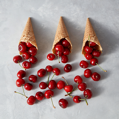 Natural freshly picked fruits cherries in waffle cones for homemade cakes on a gray background with place for text. Organic vegetarian raw eating.