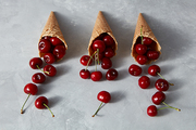 Pattern of freshly picked ripe cherries in a sweet wafer cones on a gray concrete background. Summer concept of homemade ice cream.