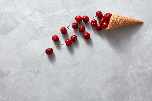 Crispy wafer cup with health organic berries cherry in a sweet cup on a gray stone background, place under text. Summer concept of homemade ice cream.