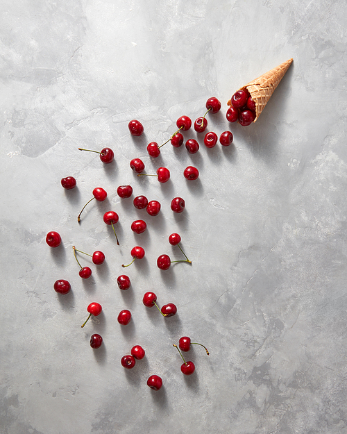 Organic cherries are poured from a waffle horn on a gray stone background with copy space. Flat lay. Summer concept of homemade ice cream