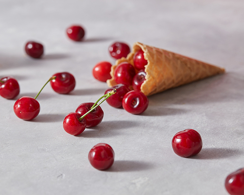 Sweet wafer cone with freshly picked red cherries on a gray background. The concept of homemade ice cream.