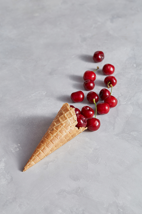 Raw ripe berry - cherries in the waffle cone for ice cream on a gray table with copy space. Top view. The concept of homemade cake.