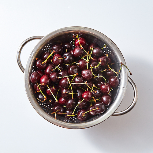 Natural organic fruits, berries - group of ripe juicy dark red cherry in the colander with water droplets on a white paper background. Top view.