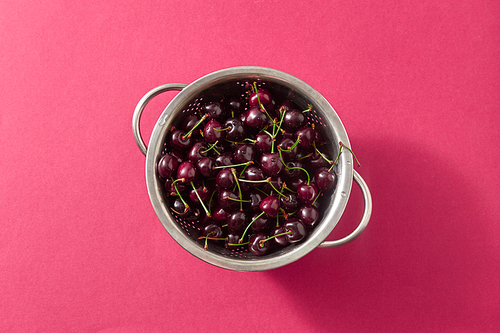 Tasty berries, freshly picked cherries in a colander with water droplets on a red background. Concept of healthy food. Copy space.