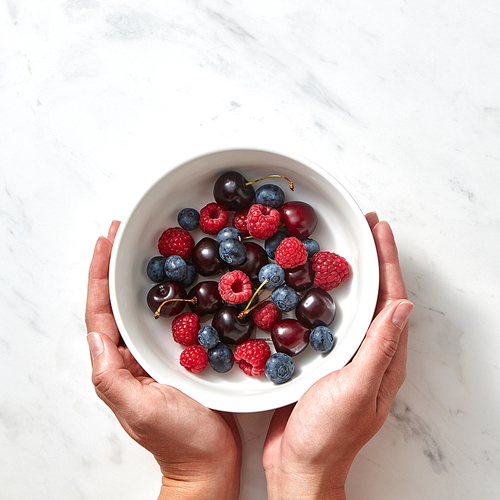 Natural organic fruits, berries in a plate on a gray stone background. Concept of healthy food with copy space. Flat lay.