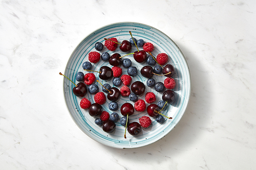 Summer tasty fruits berries on a blue plate on a gray concrete background. Concept of clean organic eating. Flat lay.