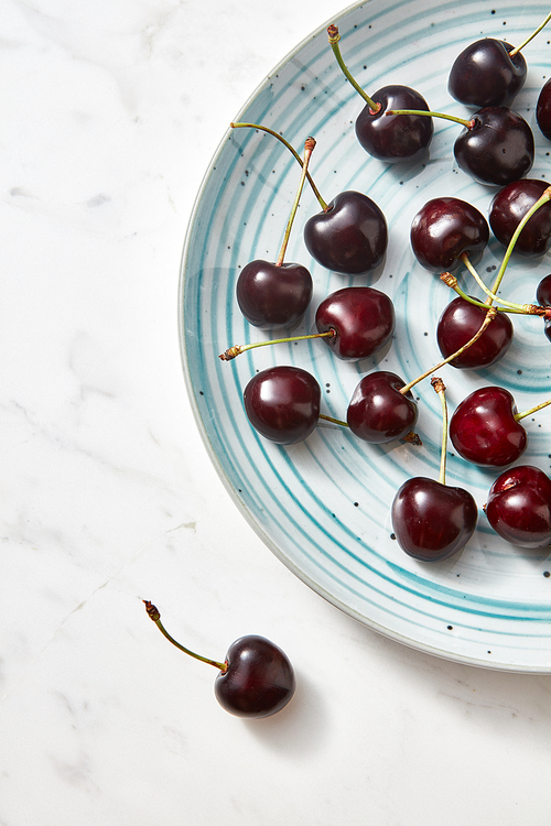 Summer tasty fruits cherries on a white plate. Sweet berries on a gray marble background. Concept of clean organic eating.