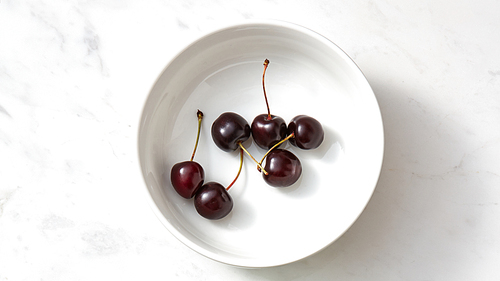 Ripe sweet cherry in the white plate on a gray background with copy space. Concept of clean organic eating. Flat lay.