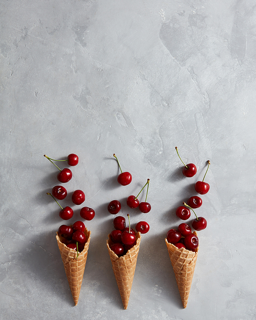 Healthy ripe red fruits cherry and waffle cups for homemade ice cream on a gray stone background with place for text. Summer organic eating. Top view.