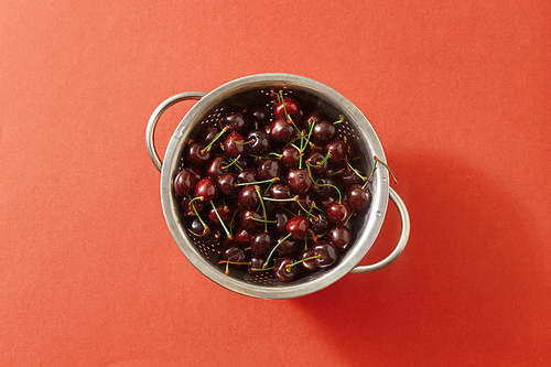 Tasty berries, freshly picked cherries in a colander with water droplets on a color background of the year 2019 Living Coral Pantone. Concept of healthy food. Copy space. Flat lay