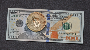 One symbolic coin of bitcoin on banknotes of one hundred dollars on dark background. Exchange bitcoin cash for a dollar.