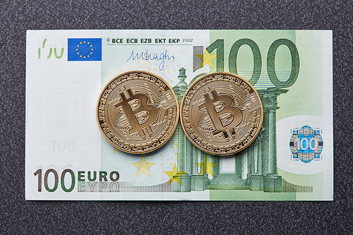 Two gold coins bitcoin on a hundred euro banknote on a dark background. Exchange bitcoin cash for a dollar. Conceptual image for worldwide cryptocurrency and digital payment system.
