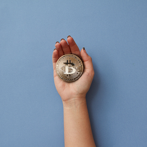 Gold coin bitcoin in a woman's hand isolated on a blue background. Cryptocurrency and blockchain concept