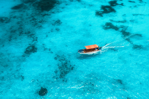 Aerial view of the fishing boat in transparent blue water at sunny day in summer. Top view from drone of floating boat in Indian ocean in Zanzibar, Africa. Landscape with yacht in clear sea. Seascape