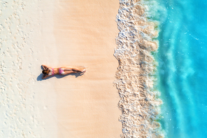 aerial view of the beautiful young lying woman on the white sandy beach near sea with waves at . summer holiday. top view of the back of sporty slim woman, clear azure water. sexy buttocks. relax