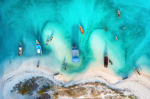Aerial view of the fishing boats in clear azure water at sunset in summer. Top view from drone of boat, sandy beach, trees. Indian ocean. Travel in Zanzibar, Africa. Landscape with sailboats, blue sea