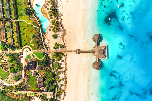 Aerial view of beautiful hotel in Indian ocean at sunset in summer. Zanzibar, Africa. Top view. Landscape with wooden hotel on the sea, azure water, sandy beach, green palm trees, pool, umbrellas