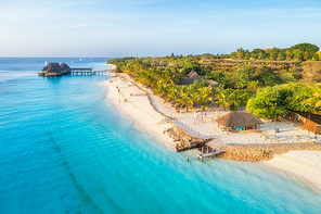 Aerial view of sandy beach of Indian Ocean at sunset. Summer holiday in Zanzibar, Africa. Tropical landscape with sea coast, palm trees, people, sand, clear blue water with waves. Top view. Seascape