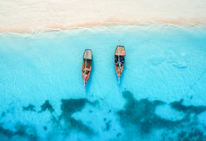 Aerial view of the fishing boats in clear blue water at sunset in summer. Top view from drone of boat, sandy beach. Indian ocean. Travel in Zanzibar, Africa. Landscape with sailboats, sea. Seascape