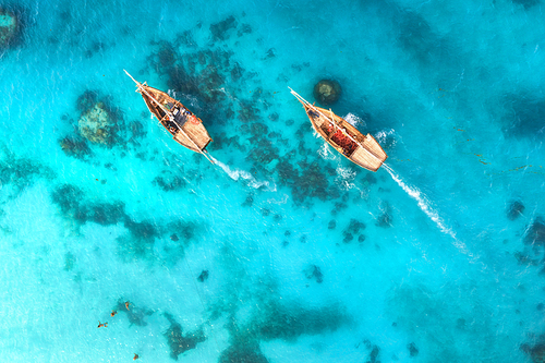 Aerial view of the fishing boats in clear blue water at sunset in summer. Top view from drone of boat, sandy beach. Indian ocean. Travel in Zanzibar, Africa. Landscape with sailboats, sea. Seascape