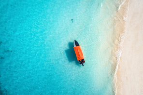 Aerial view of the fishing boat in clear blue water at sunny day in summer. Top view from drone of boat, sandy beach. Indian ocean. Travel in Zanzibar, Africa. Landscape with motorboat, sea. Seascape