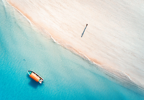 aerial view of the fishing boat in clear blue water and man on the sandy beach at  in summer. top view of boat. indian ocean. travel in zanzibar, africa. landscape with motorboat, sea. seascape