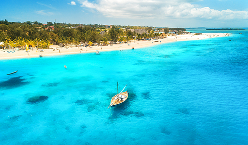 Aerial view of the fishing boat in clear blue water at sunny day in summer. Top view of boat, sandy beach, palm trees. Indian ocean. Travel in Zanzibar, Africa. Colorful landscape with sailboat, sea