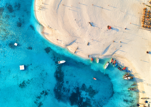 Aerial view of the fishing boats on tropical sea coast with sandy beach at sunset. Fishing village on Indian Ocean, Zanzibar, Africa. Colorful landscape with boat, clear blue water. Top view. Travel