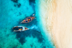 Aerial view of the fishing boats in clear blue water at sunset in summer. Top view from drone of boat, sandy beach. Indian ocean. Travel in Zanzibar, Africa. Tropical landscape with sailboats, sea