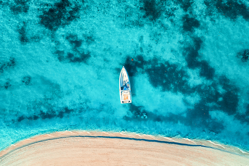 Aerial view of the white yacht in the clear blue water at sunset in summer. Top view from drone of boat, sandy beach. Indian ocean. Travel in Zanzibar, Africa. Tropical landscape with motorboat, sea