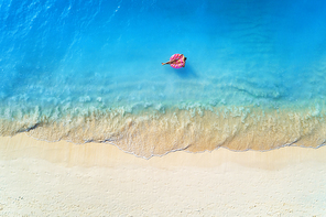 Aerial view of a young woman swimming with the donut swim ring in the clear blue sea with waves at sunset in summer. Tropical aerial landscape with girl, azure water, sandy beach. Top view. Travel