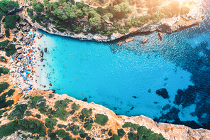 Aerial view of sandy beach with colorful umbrellas, swimming people in sea bay with transparent blue water and trees at sunrise in summer. Travel in Mallorca, Balearic islands, Spain. Top view. Nature