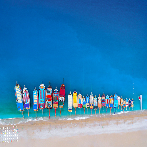 Aerial view of colorful boats in mediterranean sea in Oludeniz, Turkey. Beautiful summer seascape with ships, clear azure water and sandy beach in sunny day. Top view of yachts from flying drone