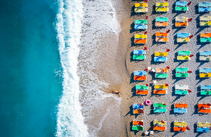 Beautiful young woman on the sea at sunrise in Oludeniz, Turkey. Aerial view of lying woman on the beach with colorful chaise-lounges. Top view from drone. Seascape with girl, azure water and waves