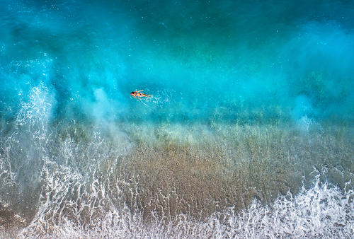 Aerial view of swimming woman in mediterranean sea in Oludeniz, Turkey. Beautiful summer seascape with girl, clear azure water, waves and sandy beach in sunny day. Top view from flying drone. Nature