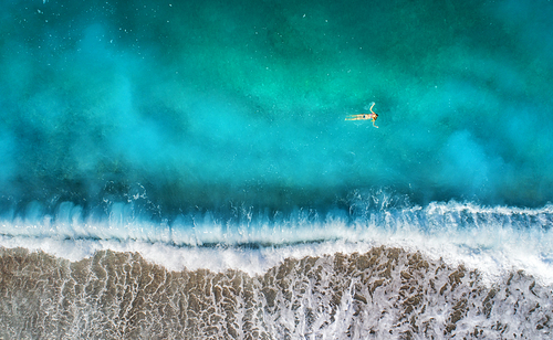 Aerial view of swimming woman in mediterranean sea in Oludeniz, Turkey. Beautiful summer seascape with girl, clear azure water, waves and sandy beach in sunny day. Top view from flying drone. Nature