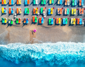 Aerial view of lying woman with swim ring in the sea in Oludeniz, Turkey. Summer seascape with girl, azure water, waves and sandy beach with colorful chaise-lounges at sunrise. Top view from drone