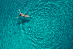 Aerial view of swimming woman in Blue Lagoon. Mediterranean sea in Oludeniz, Turkey. Summer seascape with girl, clear azure water, waves in sunny day. Transparent water. Top view from flying drone