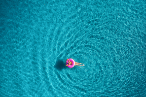 Aerial view of young woman swimming on the pink swim ring in the transparent turquoise sea in Blue Lagoon in Oludeniz,Turkey. Summer seascape with girl, azure water in the morning. Top view from drone