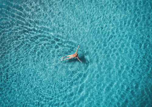 Aerial view of swimming woman in Blue Lagoon. Mediterranean sea in Oludeniz, Turkey. Summer seascape with girl, clear azure water, waves at sunrise. Transparent water.Top view from flying drone.Travel
