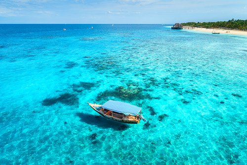 Aerial view of the fishing boat in clear blue water at sunny day in summer. Top view from the air of boat, sandy beach. Indian ocean in Zanzibar, Africa. Colorful Landscape with motorboat, clear sea