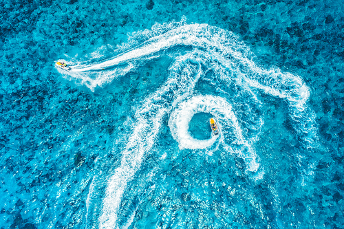 Aerial view of floating water scooter in blue water at sunset in summer. Holiday in Indian ocean, Zanzibar, Africa. Top view of jet ski in motion. Tropical seascape with moving motorboat. Extreme