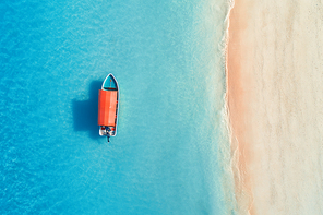Aerial view of the fishing boat in clear blue water at sunny day in summer. Top view from the air of boat, sandy beach. Indian ocean in Zanzibar, Africa. Landscape with motorboat and clear sea. Travel