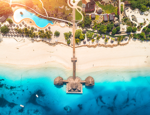 Aerial view of beautiful wooden hotel in Indian ocean at sunset in summer. Zanzibar, Africa. Top view.  Tropical landscape with building on the sea, clear blue water, sandy beach, palm trees and pool