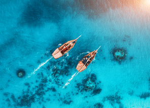 Aerial view of the fishing boats in transparent blue water at sunset in summer. Top view from drone of floating boat in Indian ocean in Zanzibar, Africa. Landscape with yacht in clear sea. Seascape