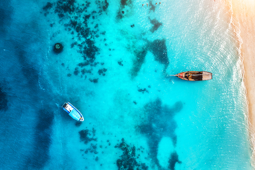 Aerial view of the fishing boats in transparent blue water at sunset in summer. Top view from of boat and sandy beach. Indian ocean in Zanzibar, Africa. Landscape with yachts and clear sea. Travel